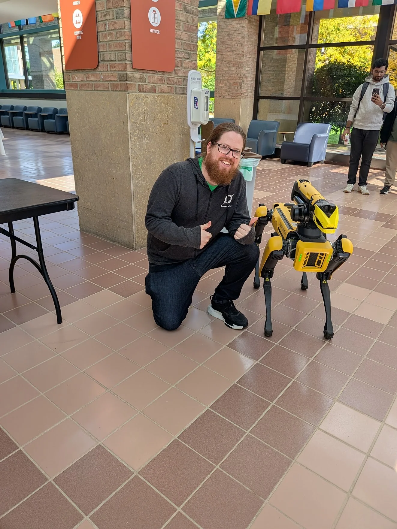 John kneeling beside Spot, the yellow Boston Dynamics quadruped robot, at MHacks.