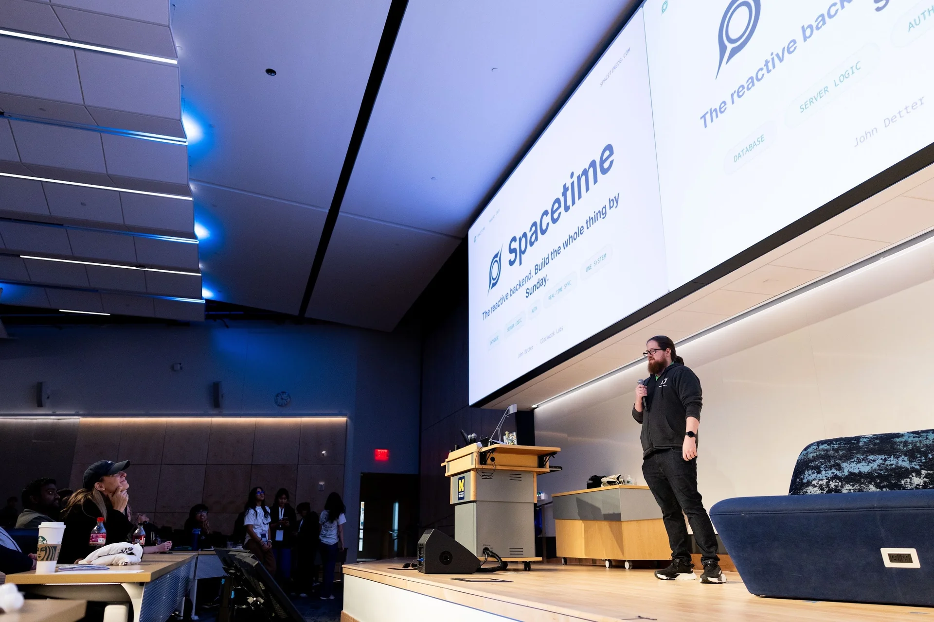 John onstage with a microphone beneath the Spacetime presentation at the MHacks opening ceremony.
