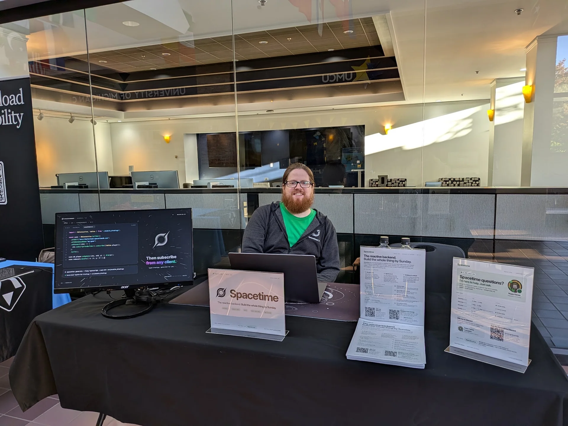 John behind the Spacetime sponsor table at Pierpont Commons, with a demo monitor, laptop, and printed guides.