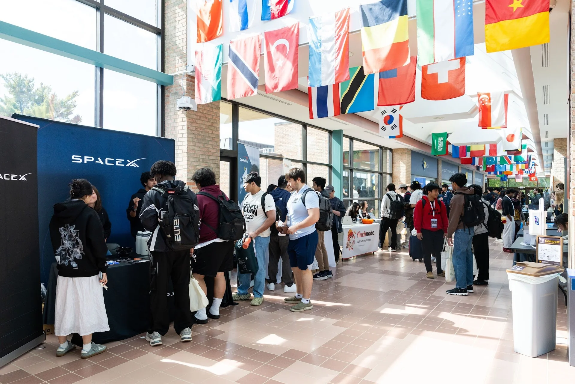 Students talking with sponsors at tables along the flag-lined hallway at Pierpont Commons.